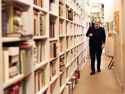 Umberto Eco caminha diante da estante de livros em sua casa.