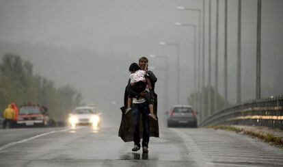 Um refugiado grita a seus companheiros para que esperem, enquanto caminha com sua filha no colo por uma estrada grega para a Macedônia.