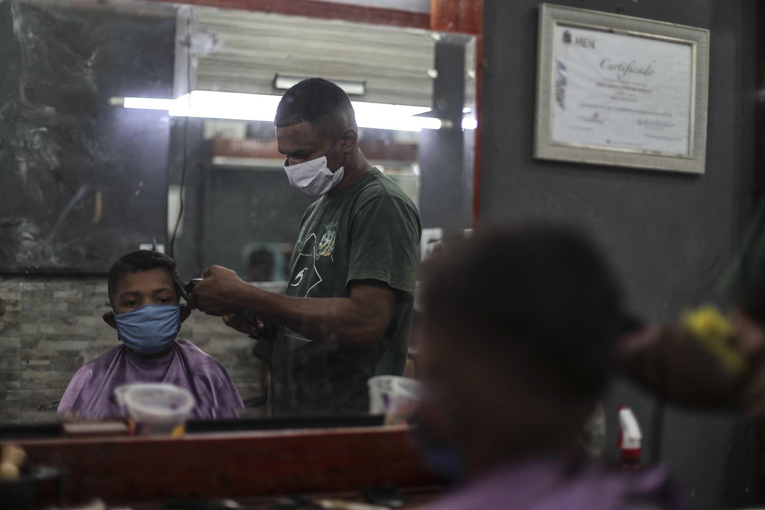 Um barbeiro da favela de Mandela, no Rio de Janeiro, trabalha com máscara de proteção durante pandemia de coronavírus.