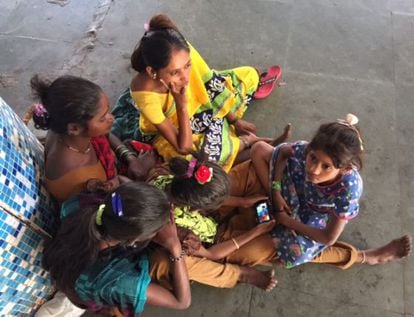 Um grupo de garotas se reúne ao redor de um telefone em uma estação de trens de Bombaim.