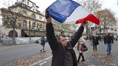 Um homem ergue a bandeira da França em frente ao Bataclan.