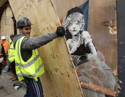 Homem cobre com uma prancha de madeira o grafite de Banksy diante da Embaixada de França em Londres.