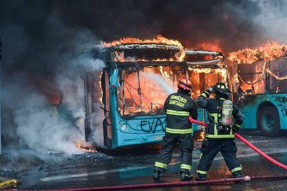 Bombeiros combatem incêndio em ônibus que foram atacados durante os protestos em Santiago.