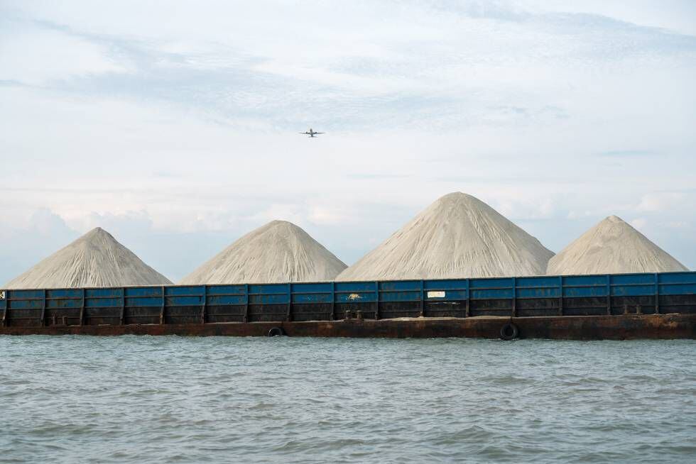 Montanhas de material para construção, provavelmente com areia misturada com granito, entram no porto ocidental de Singapura de barco.