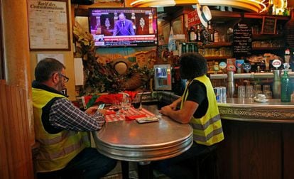 Dois coletes amarelos ouvem Philippe na televisão na quarta-feira, em um bar em Paris.