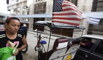 Táxi puxado por bicicleta exibe bandeiras dos EUA e de Cuba em Havana.