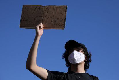 Um manifestante com uma máscara com os dizeres “não consigo respirar” segura um cartaz que faz menção aos 8 minutos e 46 segundos.