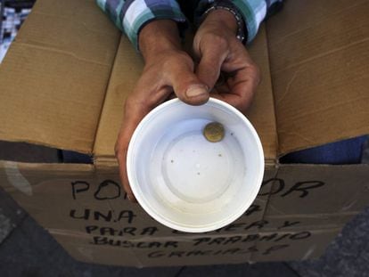 Um mendigo segura um copo de plástico enquanto pede dinheiro em Madri