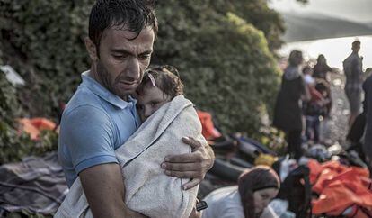 Um homem abraça e seca sua filha ao desembarcarem na ilha de Lesbos, após atravessarem parte do mar Egeu num bote de plástico.