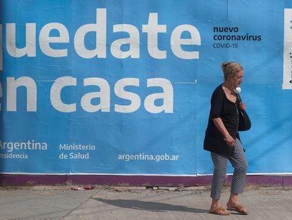 Uma mulher passa em frente a um cartaz governamental que pede à população que fique em casa.