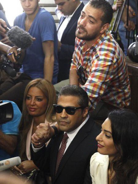 Os presos Mohamed Fahmy (centro) e Baher Mohamed (de pé, acima) falam com a imprensa ao lado da advogada Amal Clooney (direita) e da mulher de Fahmy.