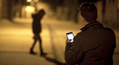 Um homem usa seu celular diante da silhueta de uma jovem.