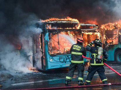 Bombeiros combatem incêndio em ônibus que foram atacados durante os protestos em Santiago.