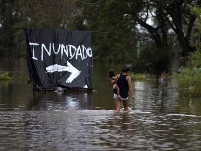 Mulher carrega bebê em área inundada na Argentina.