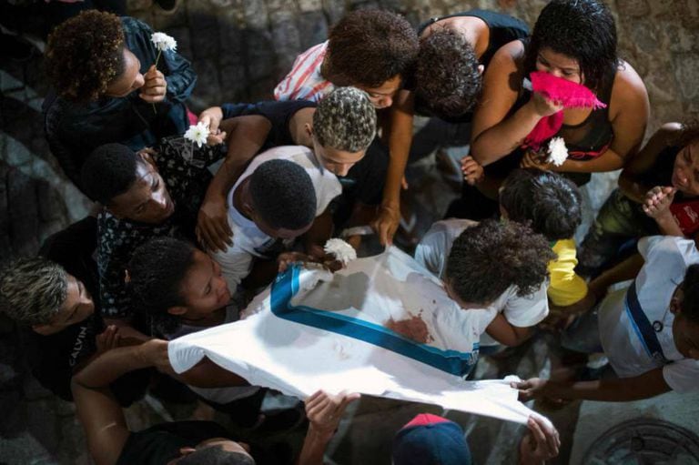 Amigos e familiares de Marcos Vinícios choram sobre sua camiseta da escola manchada de sangue, durante o seu velório.