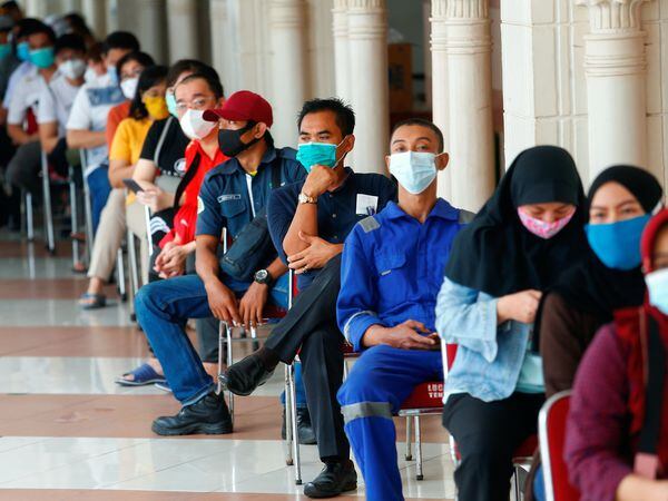 People wearing protective masks sit as they queue before receiving a dose of China's Sinovac Biotech vaccine for the coronavirus disease (COVID-19) at the Tanah Abang textile market, as Indonesia drives mass vaccination for vendors in Jakarta, Indonesia, February 17, 2021. REUTERS/Ajeng Dinar Ulfiana