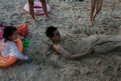 Um homem se diverte com a família enquanto uma criança o cobre com areia da praia de Xichong. 