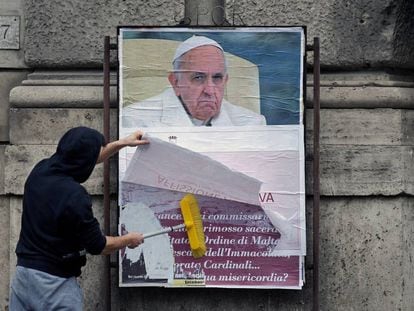 Um operário cobre um cartaz contra o Papa em uma rua de Roma.