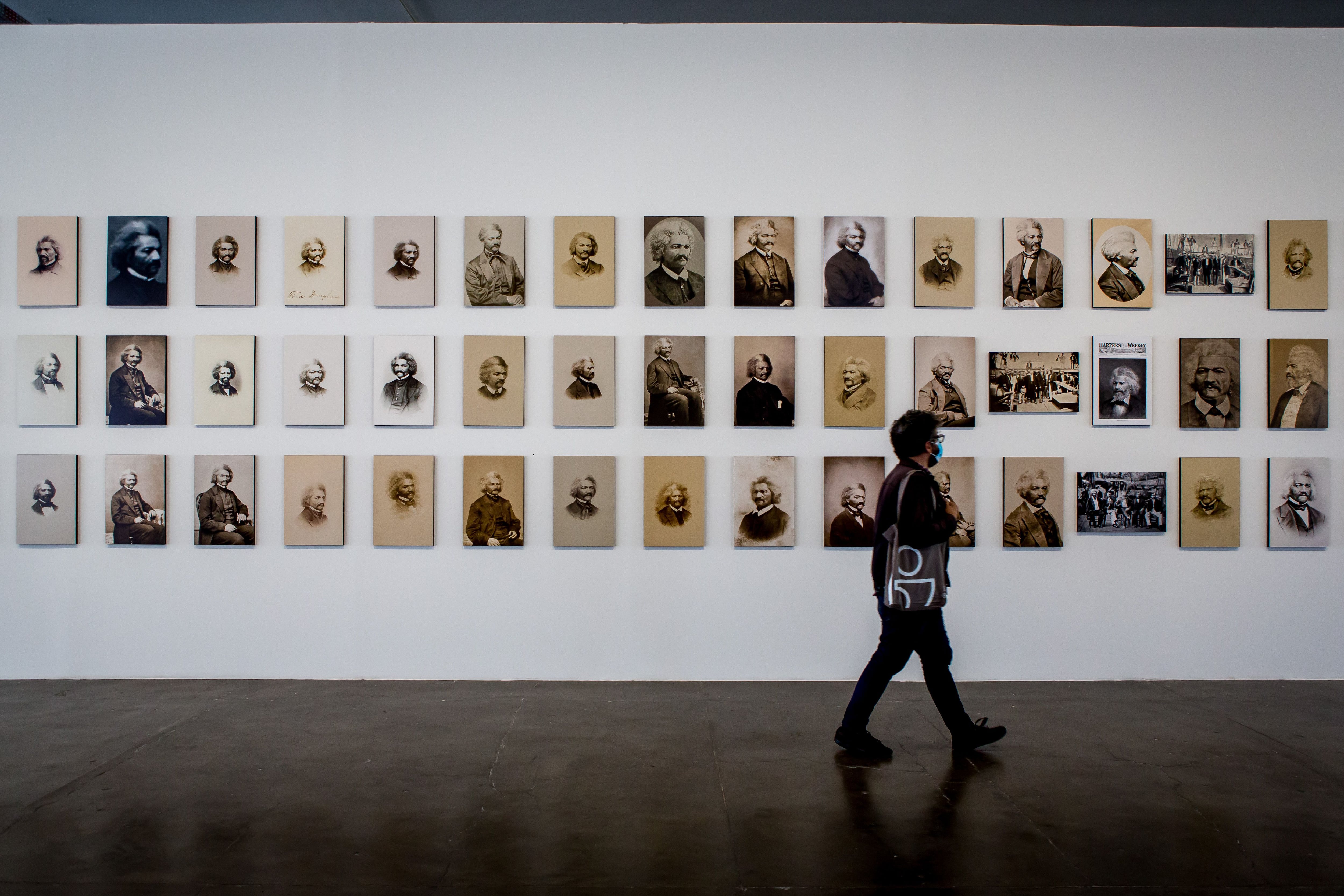 Um homem caminha em frente a uma série de retratos de Frederick Douglass na Bienal de São Paulo.