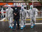 Tres médicos, de blanco, acompañan a un paciente enfermo al hospital de Wuhan, en China.