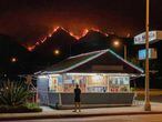 Un hombre en un restaurante mientras al fondo se ven las llamas que devoraban el jueves por la noche las colinas del Parque Nacional de Los Ángeles., el 11 de septiembre.