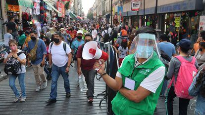 Um funcionário promove o distanciamento social em uma movimentada rua comercial do centro histórico da Cidade do México.