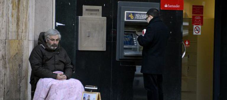 Um homem pede esmolas na porta de um caixa automático em Madri.