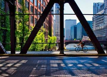 Ciclista cruzando uma rua do ‘Loop’, em Chicago (EUA), com o rio homônimo em segundo plano.
