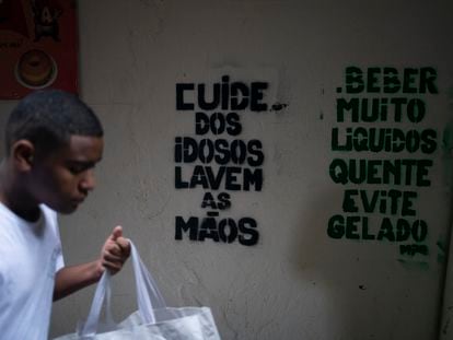 Um homem passa em frente a recados de conscientização sobre o coronavírus na Rocinha, Rio de Janeiro.