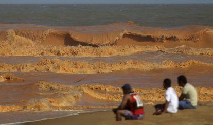 Men look on from the banks of Rio Doce (Doce River), which was flooded with mud after a dam owned by Vale SA and BHP Billiton Ltd burst, as the river joins the sea on the coast of Espirito Santo in Regencia Village, Brazil, November 22, 2015. REUTERS/Ricardo Moraes