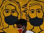 A youth wearing a facemask walk past a mural depicting people wearing famcemaks during the first day of a 21-day government-imposed nationwide lockdown as a preventive measure against the COVID-19 coronavirus, in Mumbai on March 25, 2020. - India's billion-plus population went into a three-week lockdown on March 25, with a third of the world now under orders to stay indoors, as the coronavirus pandemic forced Japan to postpone the Olympics until next year. (Photo by INDRANIL MUKHERJEE / AFP)