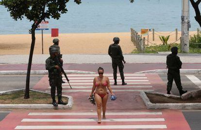 Mulher caminha na orla da praia da Costa em meio aos soldados.