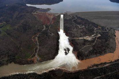A água se evade com capacidade máxima pelo deságue da represa de Oroville, na segunda-feira. À esquerda, o dique de contenção emergencial danificado.
