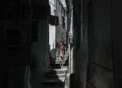 Mulher caminha por rua de favela no Rio de Janeiro.