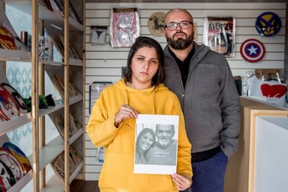 Ao lado do irmão na loja da família, Priscila segura foto do pai e da irmã mortos pela covid-19.
