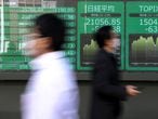 People wearing protective face masks, following an outbreak of the coronavirus, walk past a screen showing Nikkei index, outside a brokerage in Tokyo, Japan February 28, 2020. REUTERS/Athit Perawongmetha