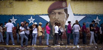 Fila em Caracas diante de um muro pintado com o rosto de Hugo Chávez.