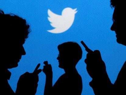 Usuários de celulares em frente ao logotipo do Twitter.
