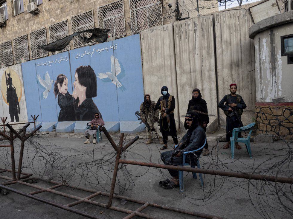 Milicianos do Talibã monta guarda em Cabul diante de um cartaz que mostra uma mulher e uma menina.