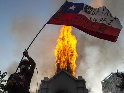 Manifestante balança bandeira chilena diante de igreja incendiada em Santiago, neste domingo.