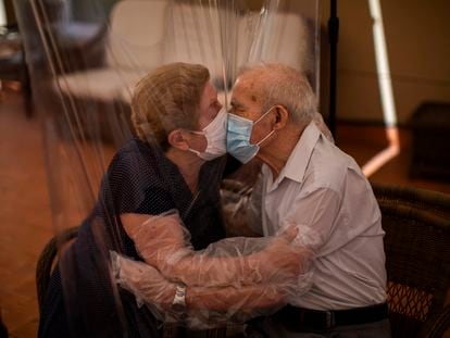 Agustina Cañamero, 81, d Pascual Pérez, 84, se beijam com a proteção de máscaras e um plástico em Barcelona.