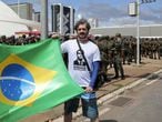 Eleitor de Bolsonaro posa com uma bandeira do Brasil diante do ensaio do esquema de segurança da posse.