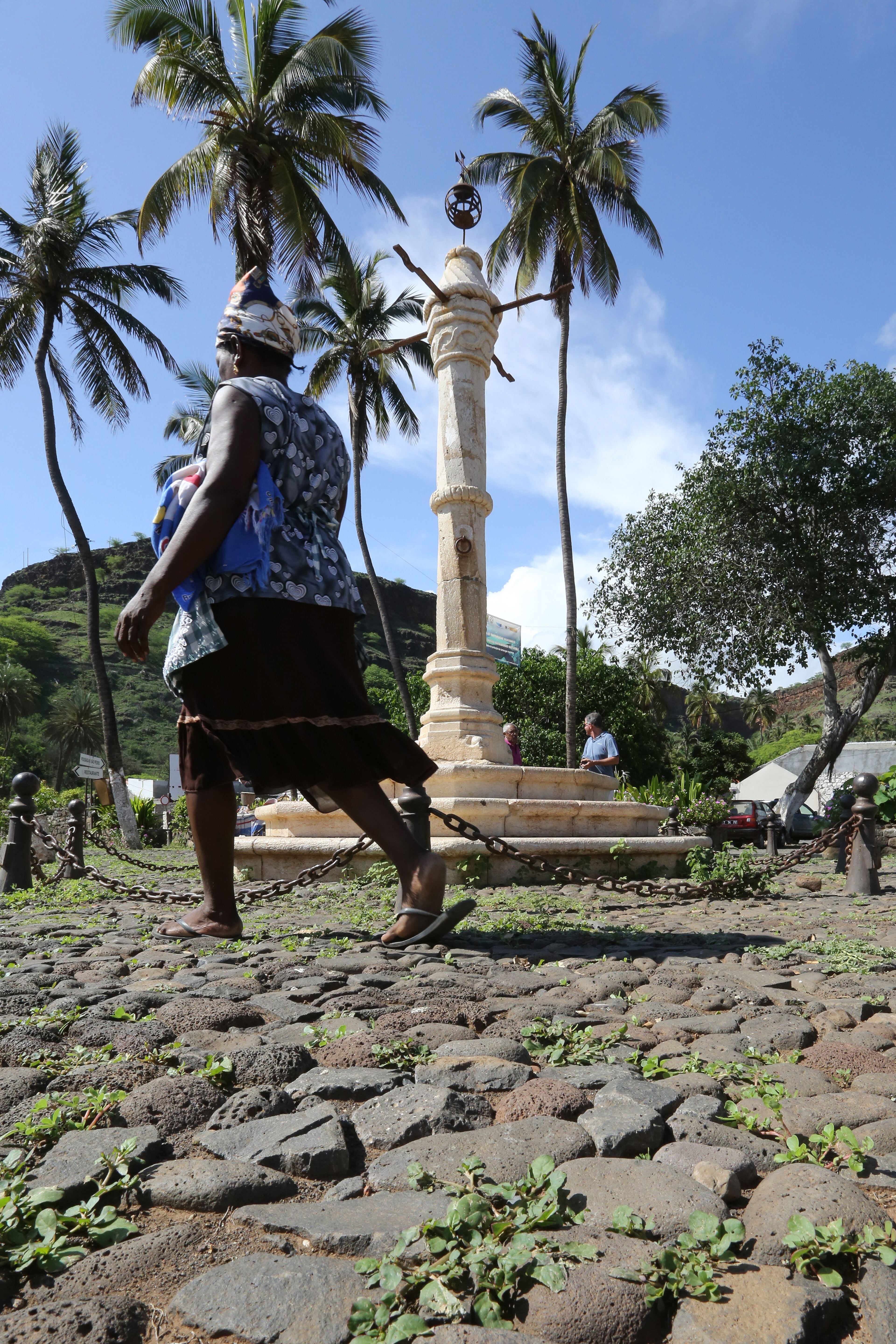 Mulher caminha em frente ao pelourinho da Cidade Velha (Cabo Verde), um lugar onde os negros escravizados eram castigados.