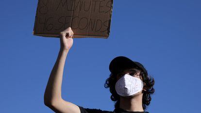 Um manifestante com uma máscara com os dizeres “não consigo respirar” segura um cartaz que faz menção aos 8 minutos e 46 segundos.
