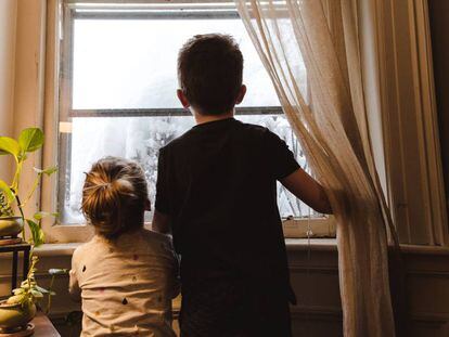 Duas crianças olham por uma janela. Quarentena impõe desafio para pais e filhos.