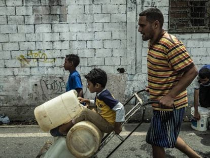 Pai e filhos carregam galões de água em Caracas