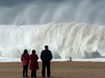 Três pessoas observam uma onda na praia do Meco, onde ocorreu a tragédia.