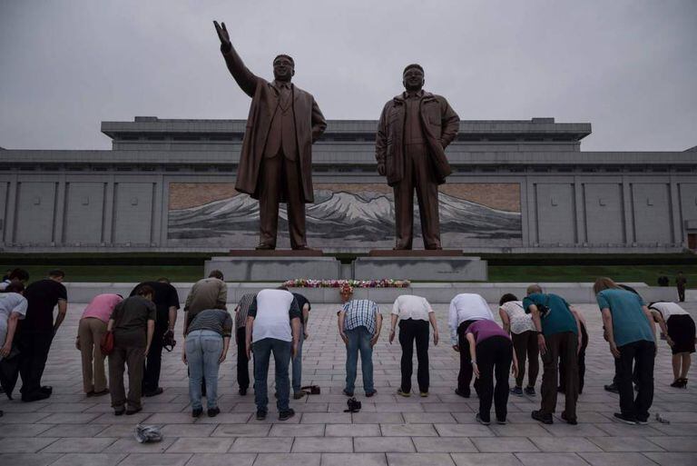 Turistas em frente a uma estátua de Kim Il-Sung (esquerda) e Kim Jong-Il (direita), em Pyongyang.