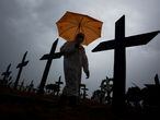 (FILES) In this file photo taken on February 25, 2021 a worker wearing a protective suit and carrying an umbrella walks past the graves of COVID-19 victims at the Nossa Senhora Aparecida cemetery, in Manaus, Brazil. - Brazil registers record of 1,641 Covid-19 deaths in 24 hours, on March 2, 2021, according to official sources. (Photo by MICHAEL DANTAS / AFP)