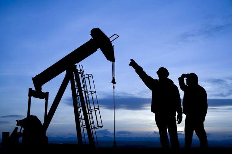 Dois trabalhadores observam um poço de extração de petróleo